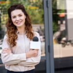 attractive female journalist holding microphone and looking at camera
