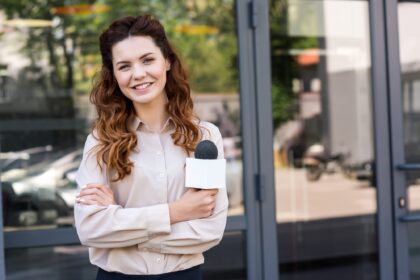 attractive female journalist holding microphone and looking at camera