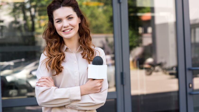 attractive female journalist holding microphone and looking at camera