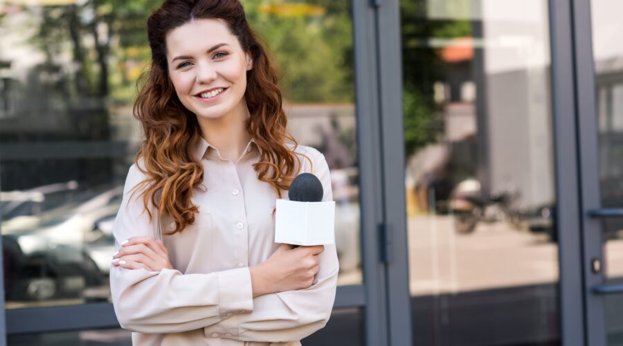 attractive female journalist holding microphone and looking at camera
