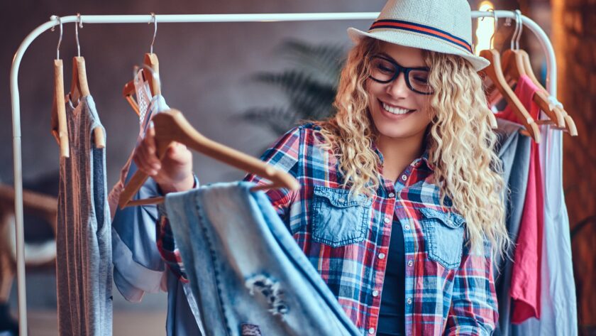 A woman chooses fashionable clothes on the coat rack.