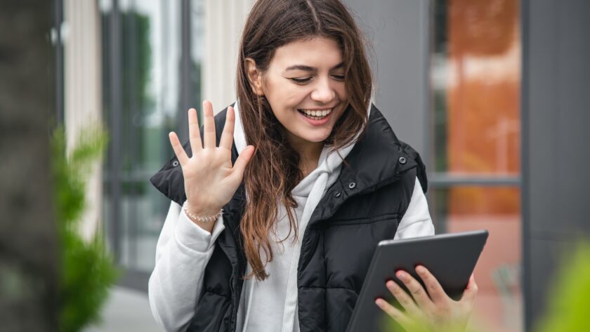 Attractive young woman uses a tablet, communicates by video call outside.