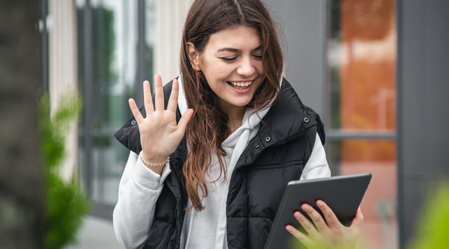 Attractive young woman uses a tablet, communicates by video call outside.