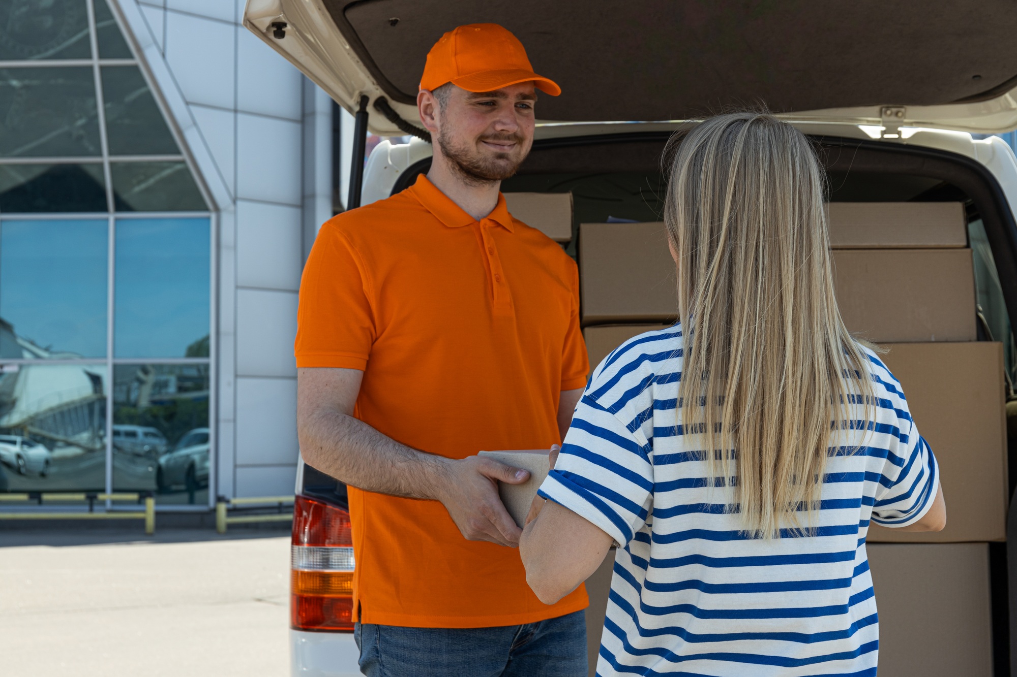 The courier gives the parcel to the client near the car with the parcels