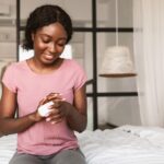 African American Lady Applying Hands Cream Moisturizing Skin In Bedroom