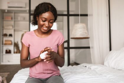 African American Lady Applying Hands Cream Moisturizing Skin In Bedroom