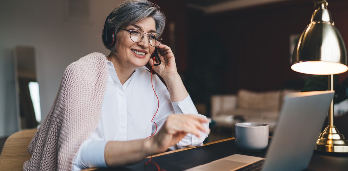 Happy mature woman with headphones and laptop at table