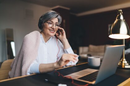 Happy mature woman with headphones and laptop at table