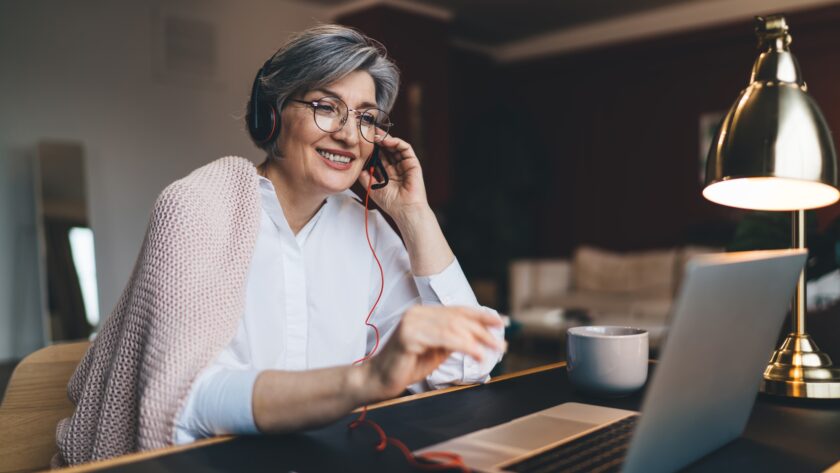 Happy mature woman with headphones and laptop at table