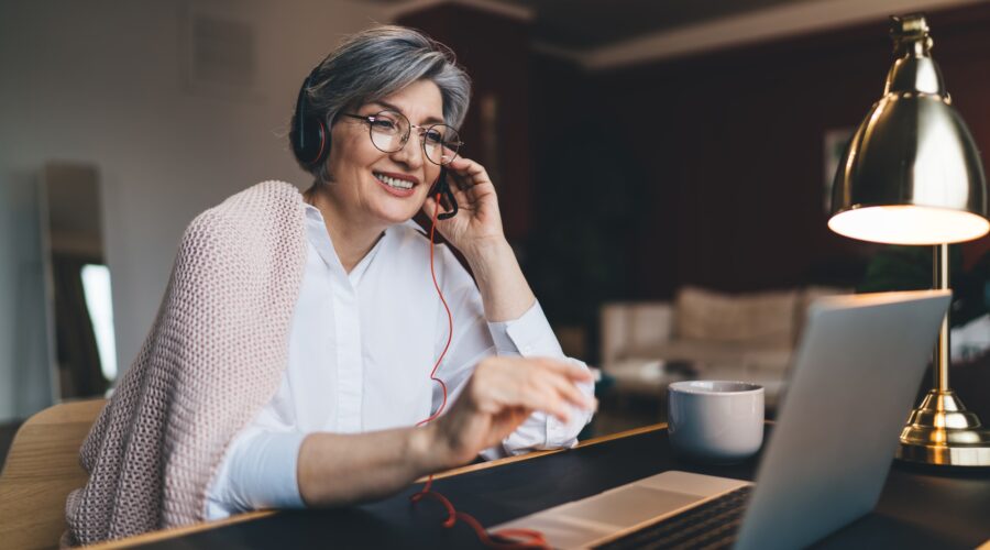 Happy mature woman with headphones and laptop at table