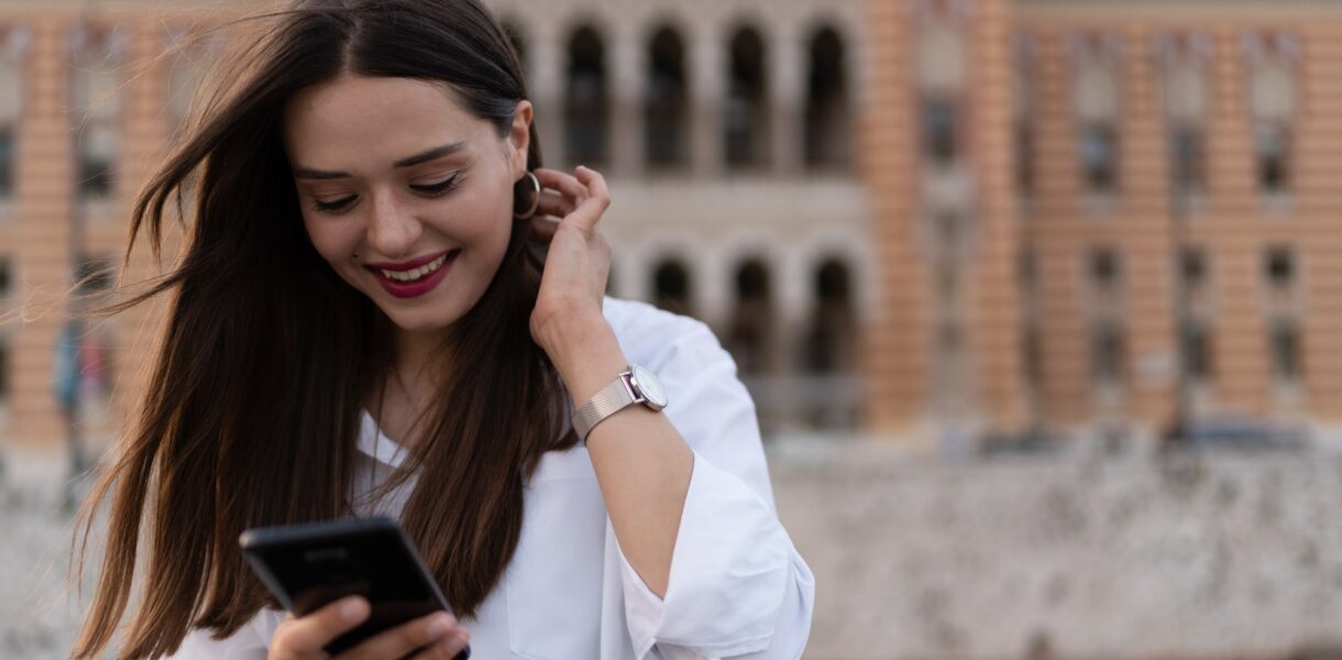 The young woman writes on the cell phone and smiles