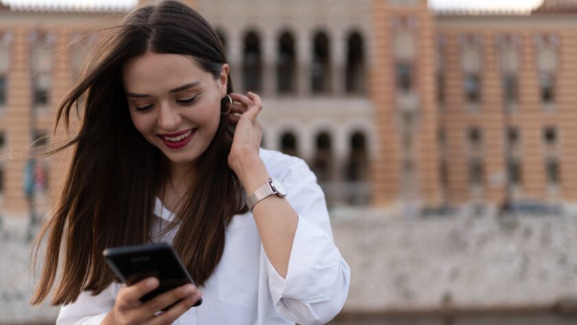 The young woman writes on the cell phone and smiles