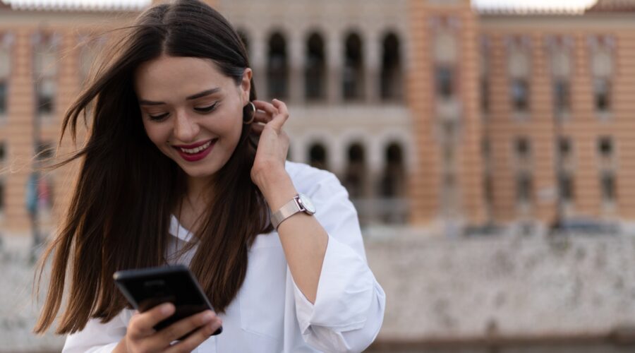 The young woman writes on the cell phone and smiles