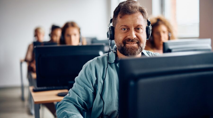 Happy mature man e-learning on desktop PC during computer class and looking at camera.