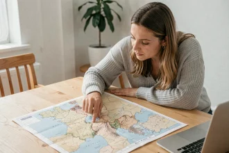 Femme consultant une carte de France imprimée posée sur un bureau en bois dans un bureau à domicile
